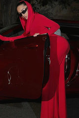 Woman in a red hooded dress leaning on the open door of a red car.