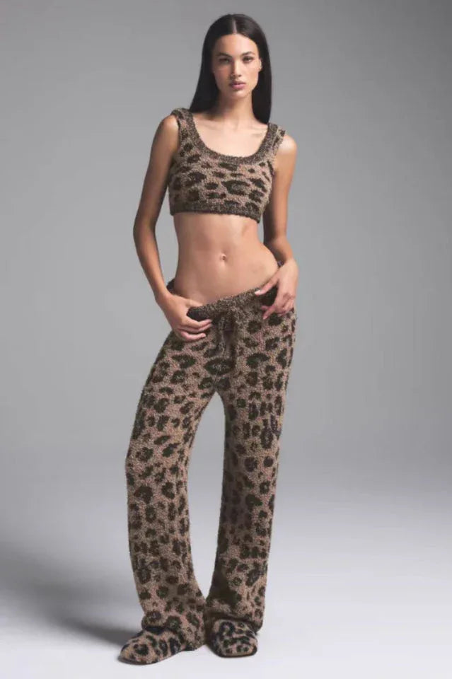 Woman wearing a leopard print fuzzy crop top and pants with slippers.