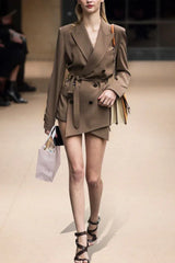 Full body shot of a model walking in a brown double-breasted blazer with a belted waist and asymmetrical hem.