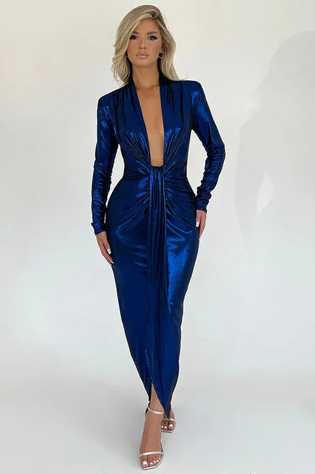 Woman wearing a long-sleeved, metallic blue, floor-length dress with a deep V-neckline and a high slit.