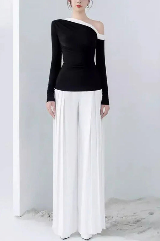 Model wearing a black long-sleeved top with an asymmetrical neckline and white wide-leg pleated pants.