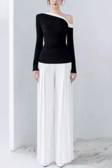 Model wearing a black long-sleeved top with an asymmetrical neckline and white wide-leg pleated pants.