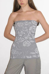 Young woman with hands behind her back wearing a light gray strapless top with a white floral pattern and vertical ribbing, paired with gray cargo pants.