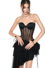 Close-up of a woman wearing a black strapless corset dress with an asymmetrical ruffled skirt and tulle detailing.