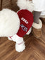 Close-up of the back of a white poodle wearing a red baseball jacket with 'New York 1988' on the back.