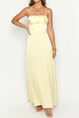woman wearing a pale yellow satin maxi dress with spaghetti straps and a sweetheart neckline, standing with one hand on hip