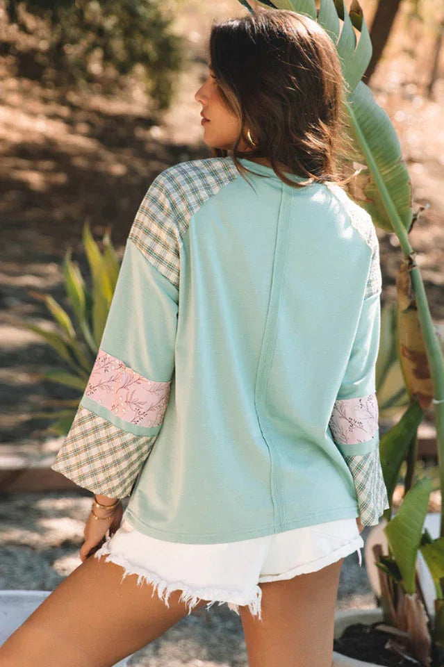 Back view of a woman wearing a mint green long-sleeved top with a heart applique and plaid patchwork sleeves.