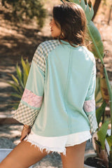 Back view of a woman wearing a mint green long-sleeved top with a heart applique and plaid patchwork sleeves.