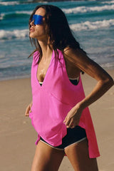 Woman in a pink V-neck tunic and black shorts on a beach, looking to the side