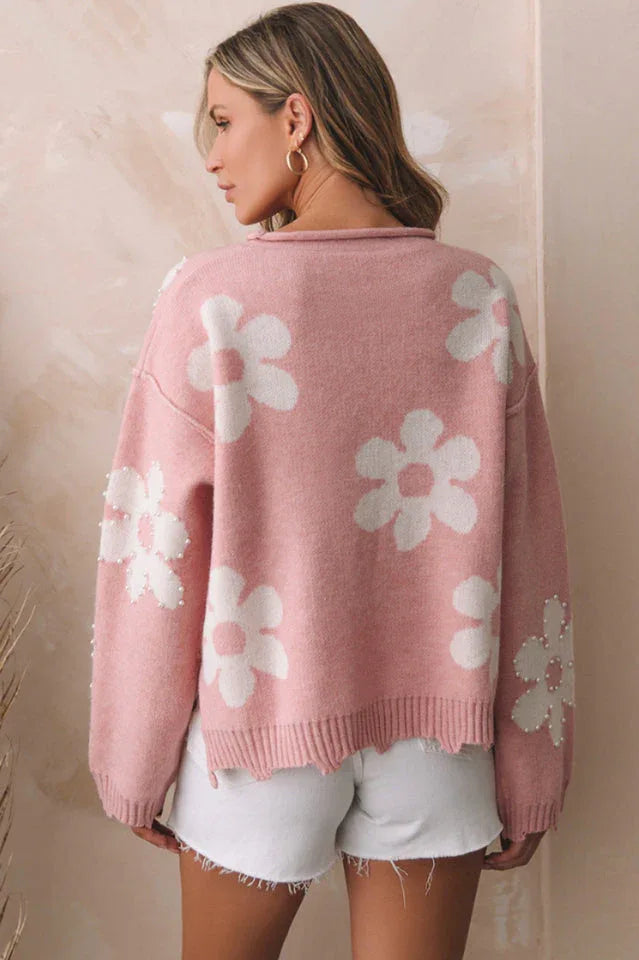 Back view of a woman wearing a pink knit sweater with a flower pattern and pearl embellishments.