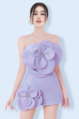 A model wearing a lavender strapless mini dress with large floral appliques on the bust and hip, adorned with sparkling embellishments at the center of each flower.