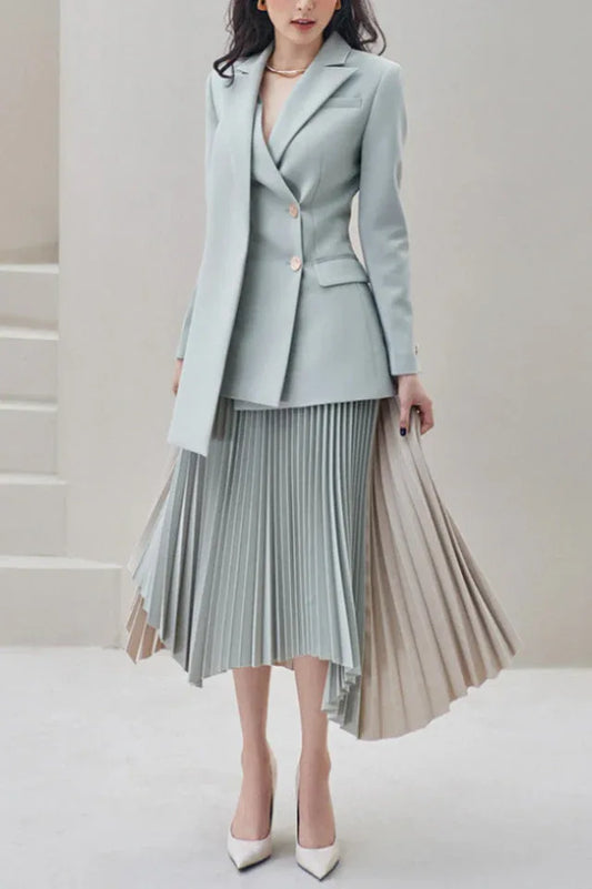 Woman wearing a light blue blazer and asymmetrical pleated skirt, standing.