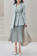 Woman wearing a light blue blazer and asymmetrical pleated skirt, standing.