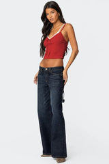 Full body side view of a woman wearing a red cropped tank top with lace trim and dark wash wide-leg jeans.