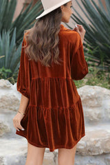 Back view of a woman wearing an orange velvet babydoll dress, highlighting the tiered design and puff sleeves.