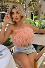 Close-up of a woman in a pink strapless feather crop top and denim shorts sitting outdoors