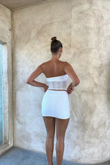 Rear view of a woman wearing a white strapless textured knit top with a twisted bust and cut-out detail, paired with a matching white textured knit mini skirt.