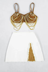 Product flat lay of a brown chain-and-bead embellished bralette top and a white high-slit skirt with fringe and pearl accents.