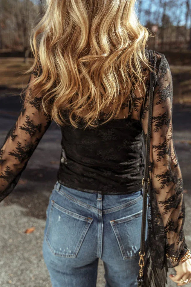 Back view of a woman wearing a black lace long-sleeved top with a scoop neckline and bell sleeves, paired with blue denim jeans.