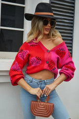 Woman wearing a red and pink colorblock strawberry print knit cardigan with a V-neckline and button-up closure.