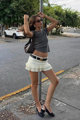 Model wearing a white pleated mini skirt with a grey t-shirt, black belt, and black slingback heels.