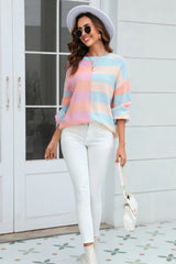 Woman wearing a pastel striped color-block knit sweater, white pants, and a white handbag