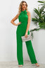 Woman posing in a green halter neck jumpsuit with a bow detail at the neckline, holding a clutch bag