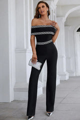 Front view of a woman in a black off-the-shoulder jumpsuit with geometric trim.