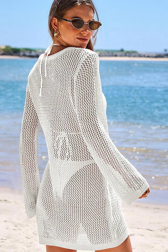 Back view of a woman wearing a white knit beach cover-up on the beach.
