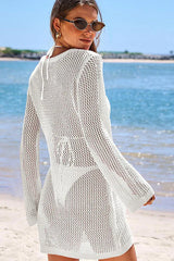 Back view of a woman wearing a white knit beach cover-up on the beach.