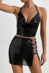 Woman wearing a black metallic mesh halter top with a cowl neckline and a matching mini skirt with a lace-up side.