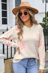Woman wearing a cream-colored knit sweater with a pink floral print, blue jeans, and a tan fedora hat.