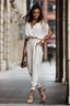 Woman wearing a light-colored off-the-shoulder jumpsuit with a deep V-neck and tie shoulder straps, walking outdoors.