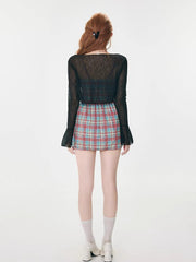 Back view of a woman wearing a plaid mini dress and a sheer black cardigan.