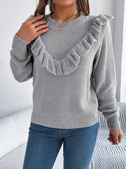 close-up of a woman wearing a grey knit sweater with ruffle trim and blue jeans