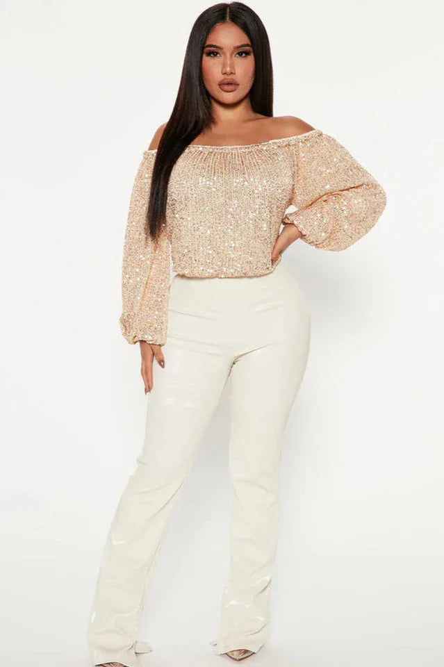 Full body shot of a woman wearing a champagne sequined off-the-shoulder top with balloon sleeves and white pants