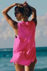 Rear view of a woman in a pink V-neck tunic on a beach, tying her hair