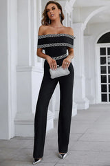 Woman wearing a black off-the-shoulder jumpsuit with geometric trim and a silver clutch.
