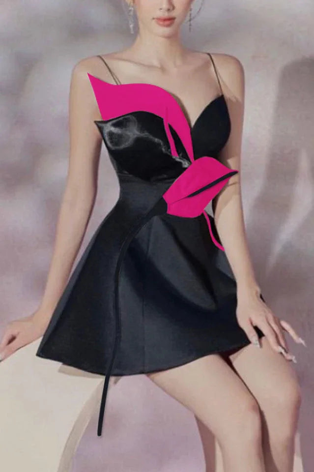 Model sitting in a black mini dress featuring a bold floral applique and spaghetti straps