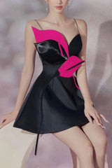 Model sitting in a black mini dress featuring a bold floral applique and spaghetti straps