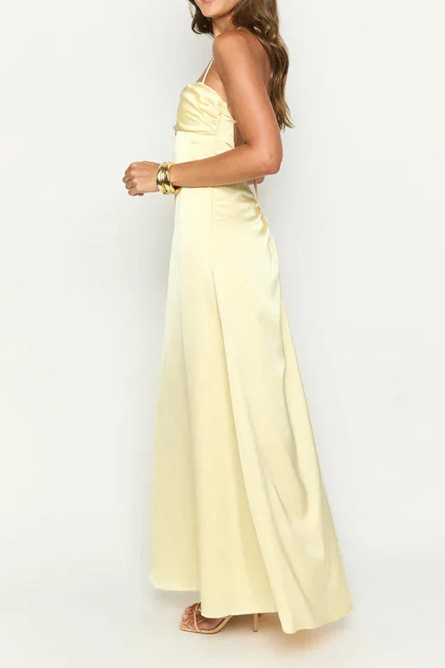 side view of a woman wearing a pale yellow satin maxi dress with spaghetti straps and a sweetheart neckline, showing the slit