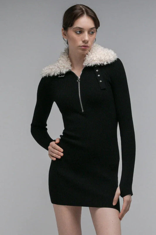 Woman wearing a black long-sleeved ribbed knit dress with a white fur-trimmed collar and a partial zipper closure.