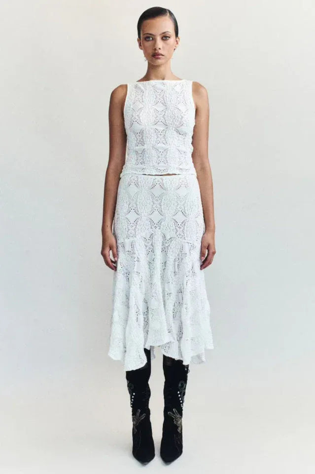 Woman wearing a white crochet knit cropped tank top and a white crochet knit asymmetrical hem midi skirt with black boots.