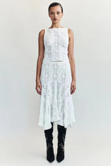 Woman wearing a white crochet knit cropped tank top and a white crochet knit asymmetrical hem midi skirt with black boots.
