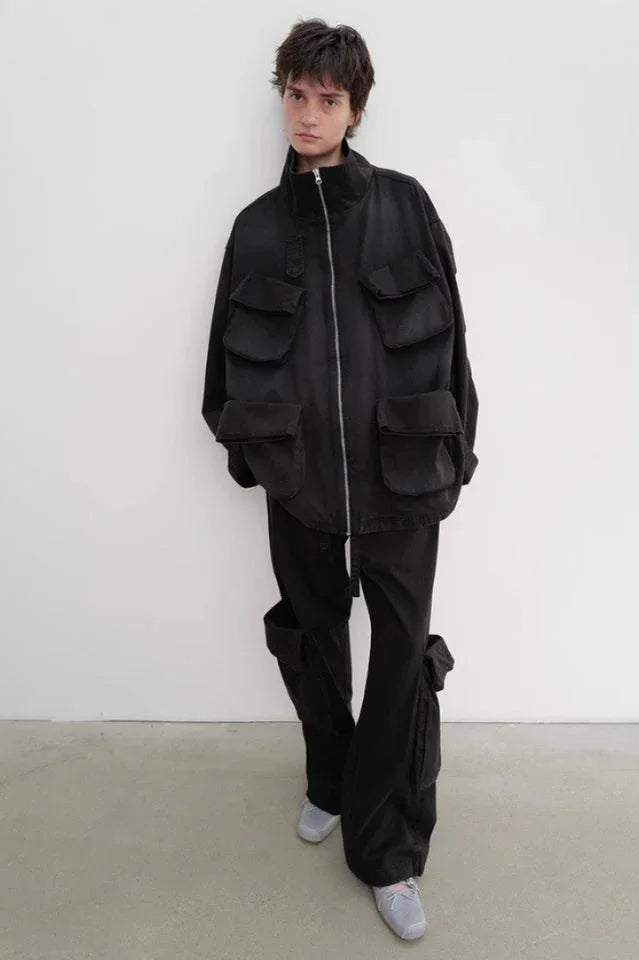 Person wearing a black oversized utility jacket with multiple pockets, black baggy cargo pants with prominent side pockets, and light grey sneakers.