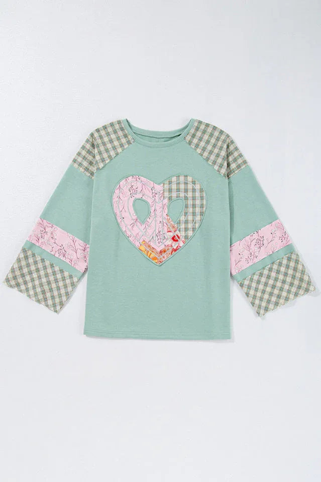 Flat lay of a mint green long-sleeved top with a heart applique and plaid patchwork sleeves.