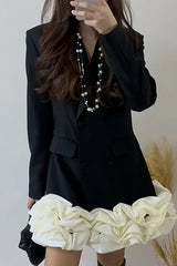 Woman wearing a black double-breasted blazer dress with a white ruffled hem and pearl necklace