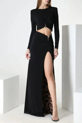 Woman wearing a black long-sleeve crop top and a black maxi skirt with a high slit and leopard print lining, posed between white cubes.