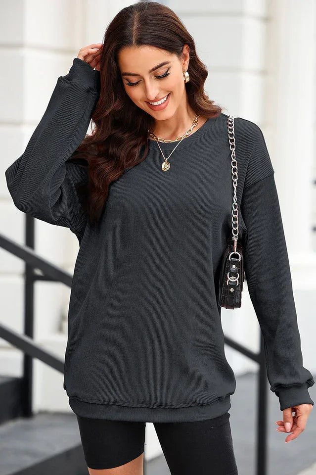Woman wearing a charcoal ribbed long-sleeve oversized tunic and black shorts, with a gold necklace and chain handbag