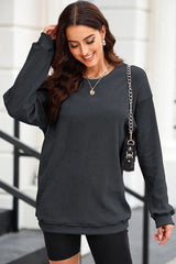 Woman wearing a charcoal ribbed long-sleeve oversized tunic and black shorts, with a gold necklace and chain handbag